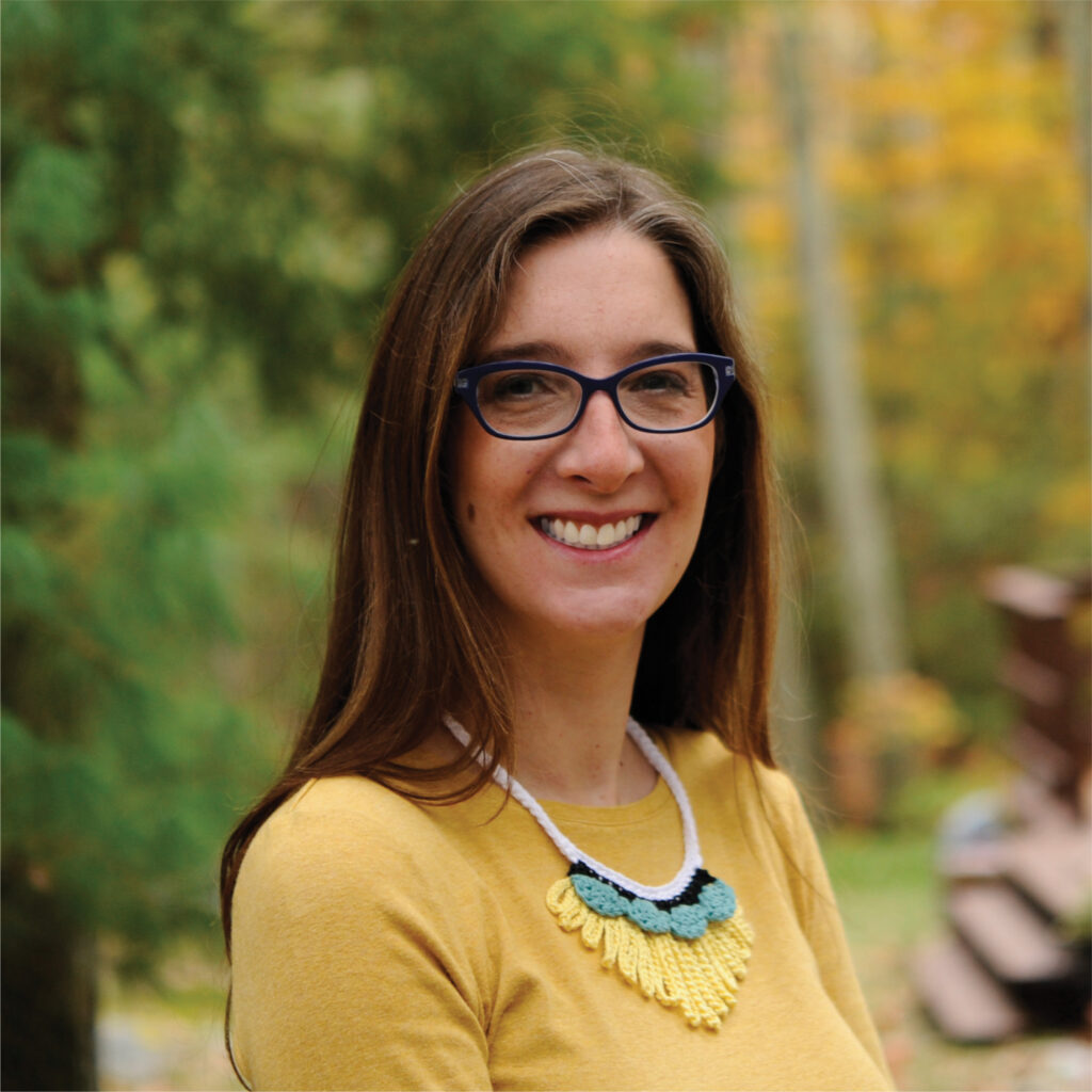 A woman smiling wearing a crochet necklace.  Have you crocheted a necklace before?  Consider this pattern your next new adventure.