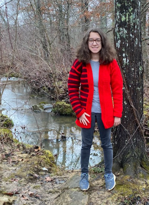 Tester Joanne wearing a red version of the Stripe Blocked Crochet Cardigan pattern in the woods.