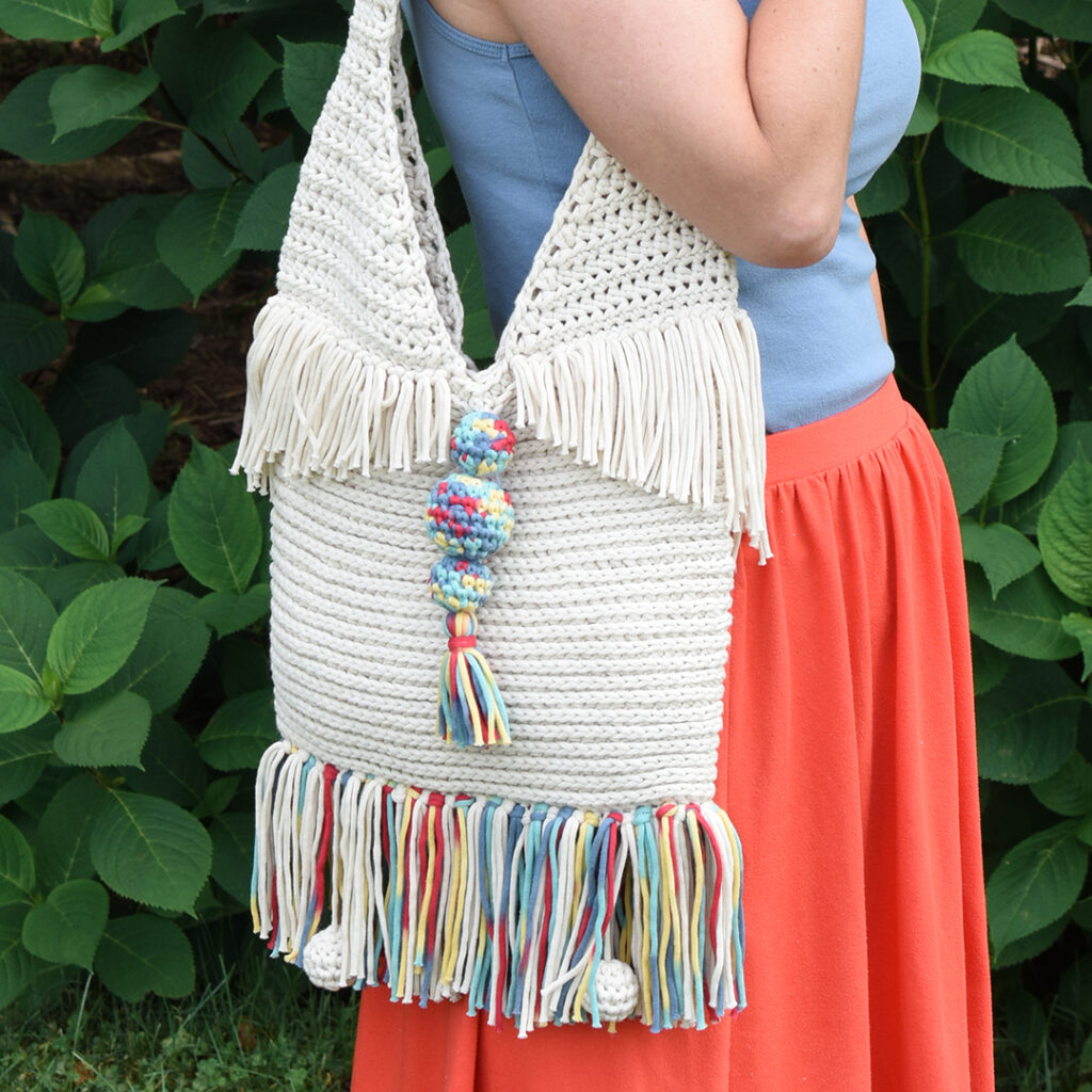 The Super Sunny Crochet Tote pattern's beautiful stitch, funky tassels, shaped fringe, and decorative balls will bring you sunshine on even the cloudiest of days.