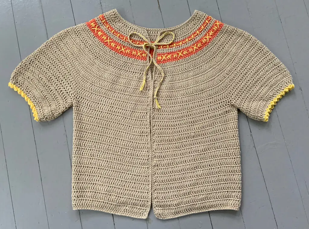 The In Stitches Cardigan laying on the floor.  This short sleeve cardigan is worked from the top down and has an embroidered yoke.