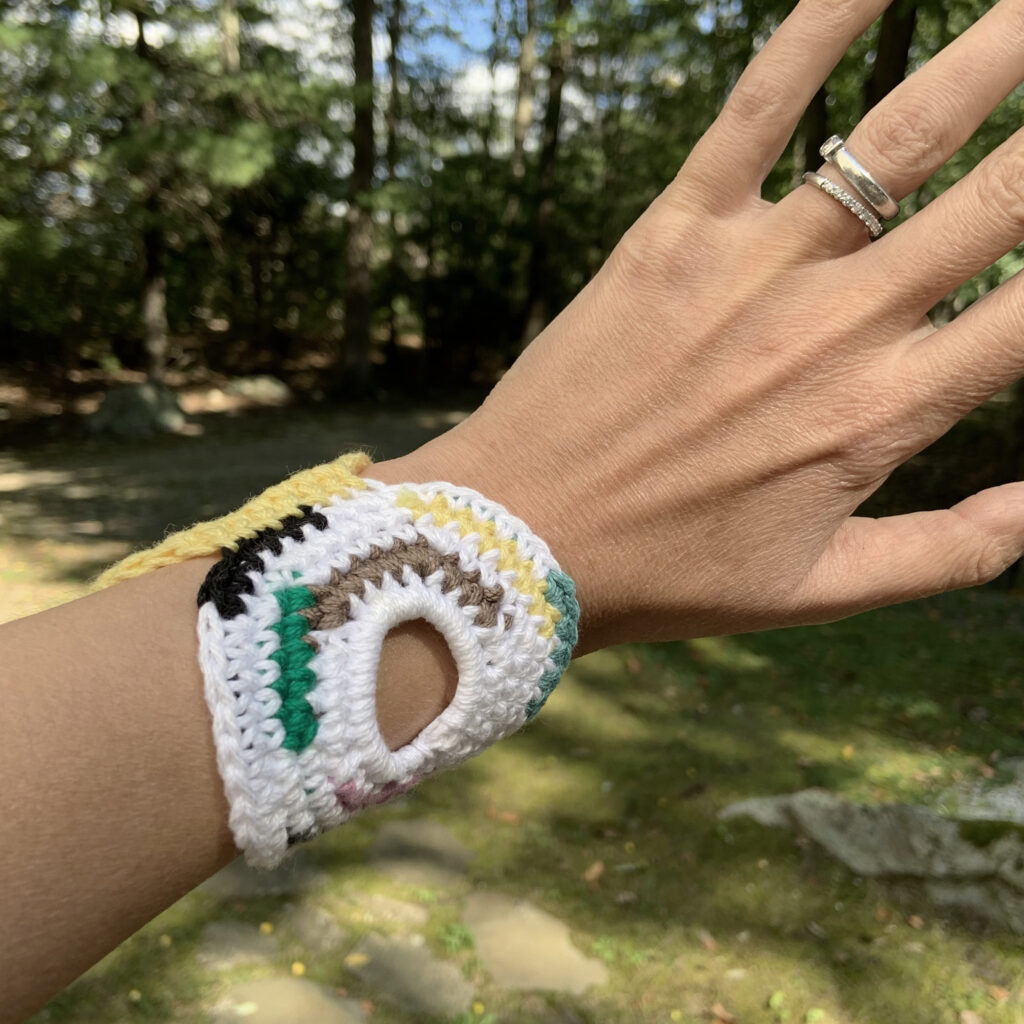 Woman's hand with a crochet bracelet in front of trees.
