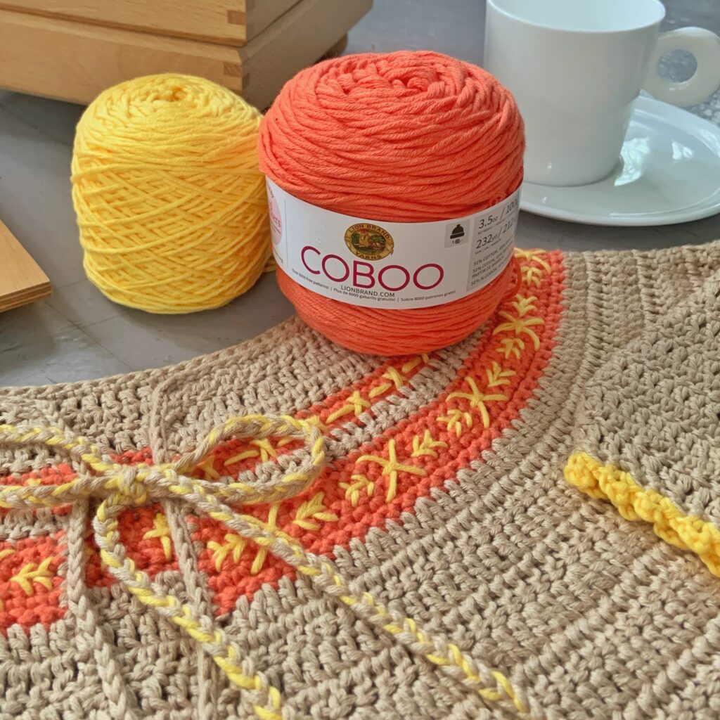 Two skeins of Coboo yarn on top of a crochet garment made with Coboo yarn.