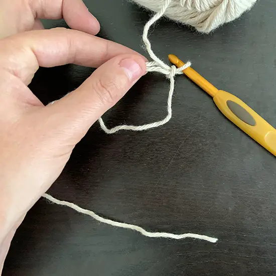 A person's hand pinching the area where the yarn crosses over of a magic crochet circle.