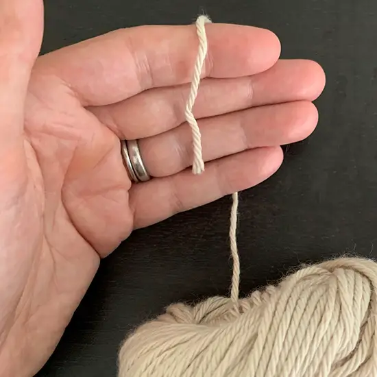 A hand holding a tail from a skein of yarn.