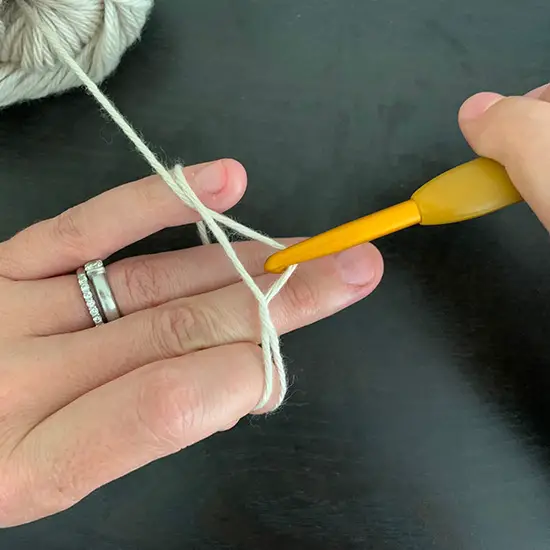 A crochet hook pulling the first strand of yarn under a second strand of yarn to create a crochet magic ring.