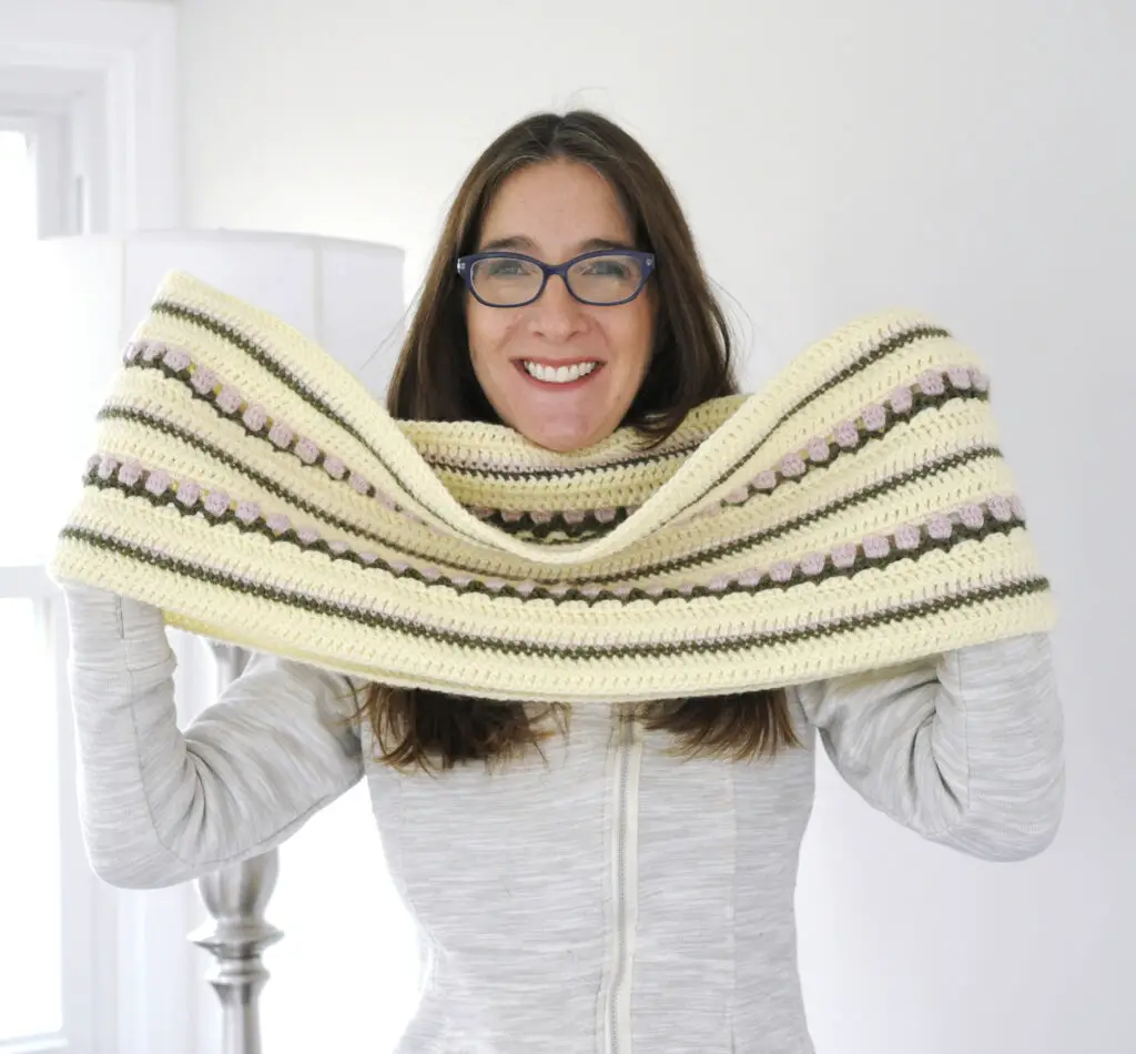 Mary Beth of Crochet with Mary Beth holding up the Roses on Repeat Crochet Infinity Scarf. The scarf is long and can wrap around the neck twice providing maximum warmth.