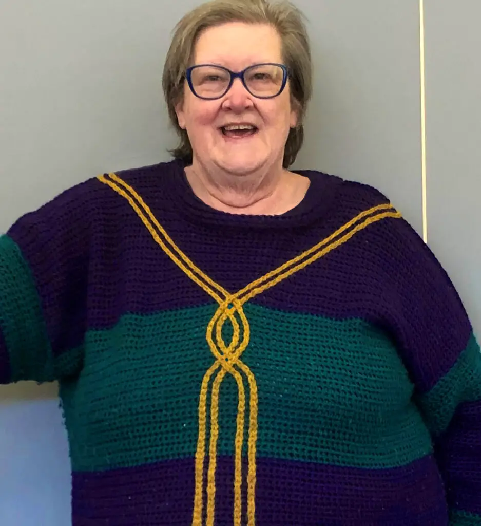 A woman wearing a crochet sweater pattern featuring a gold slip stitch cable on a blue and green crochet sweater.