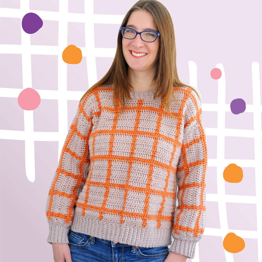The Fair and Square Crochet Sweater Pattern is a unique and modern crochet pullover. The grid pattern is made with tapestry crochet in orange and purple.