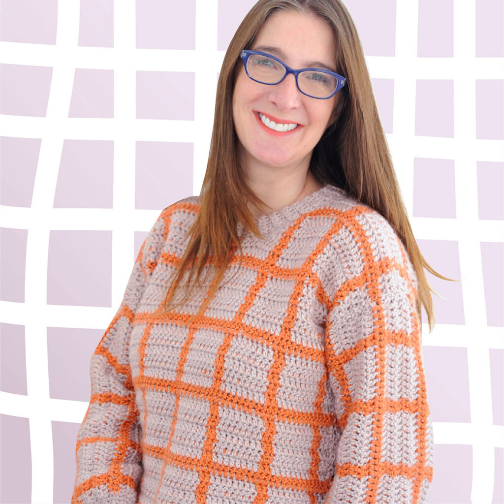 A woman wearing a grid crochet sweater.  The grid pattern is made out of orange and purple tapestry crochet in double crochet.
