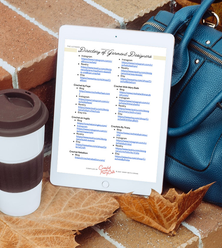 The guide can be downloaded on any device.  A tablet featuring an alphabetic page from the ultimate directory of crochet garment designers.  The tablet is on a step with a backpack, coffee cup and leaves.