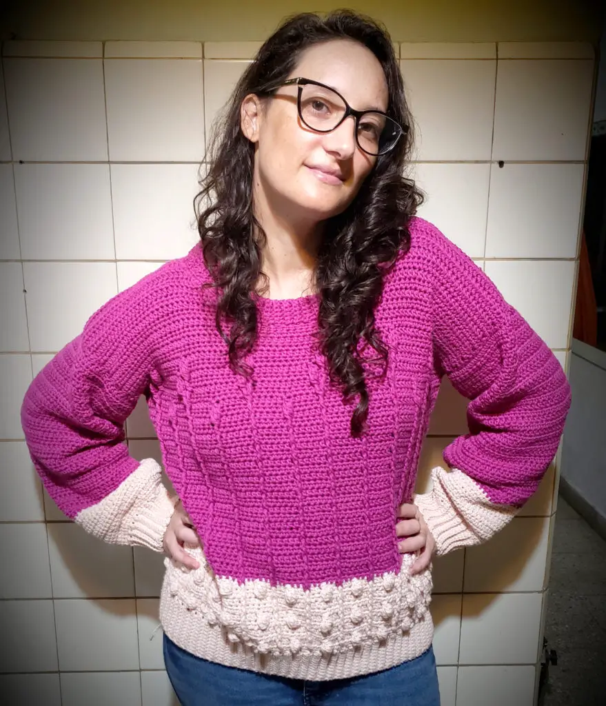 A woman wearing a magenta and light pink sweater with cables and bobbles.