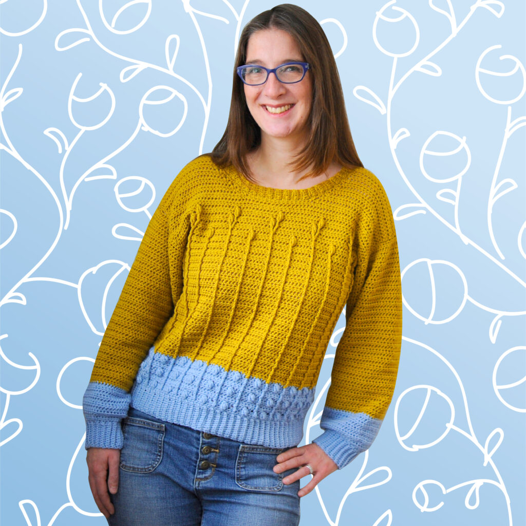Woman wearing a gold and light blue crochet sweater made from the pattern Best Buds Sweater as seen on Crochet with Mary Beth.