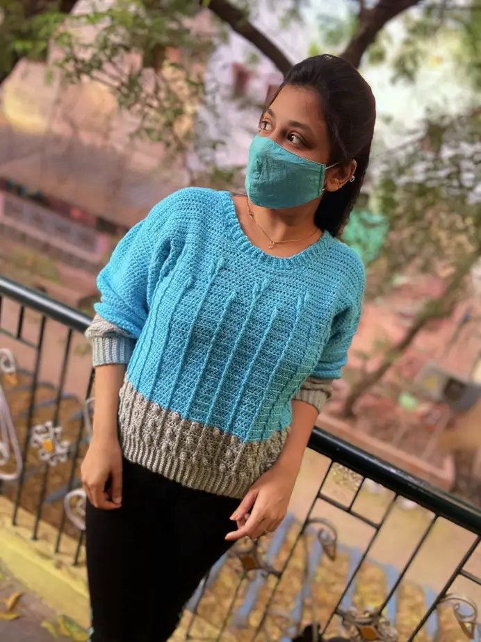 A woman wearing a blue and gray sweater made from the modern crochet pattern, Best Buds Sweater.