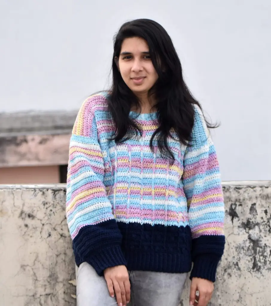 A woman wearing a variegated and navy sweater featuring a floral cable pattern made with front post cable stitches and bobble stitches.