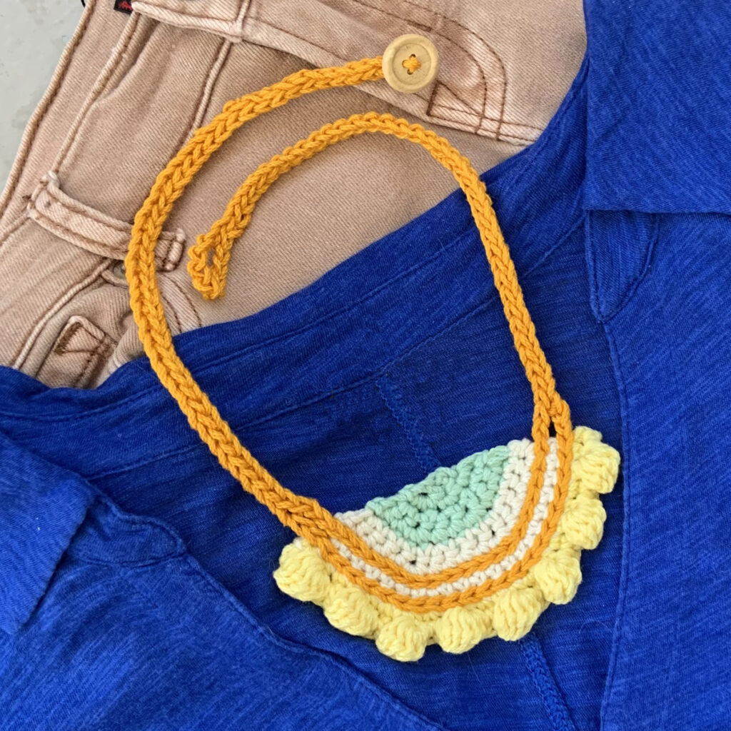 A crochet necklace pattern show on a blue shirt. The crochet jewelry pattern makes a quick crochet gift.