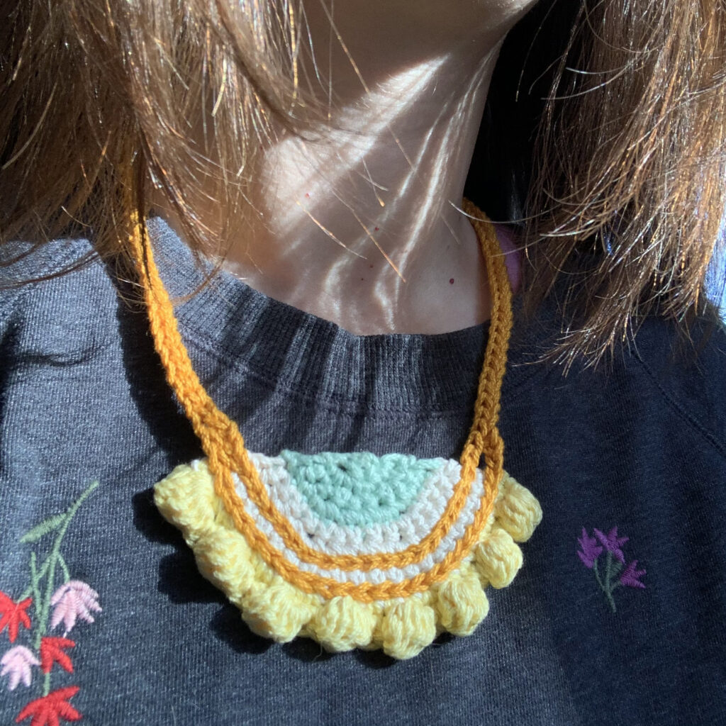 The Eight Bobble Crochet Necklace Pattern is a quick crochet project.  It is made with worsted weight yarn and shown here in blue, white, yellow, and gold.