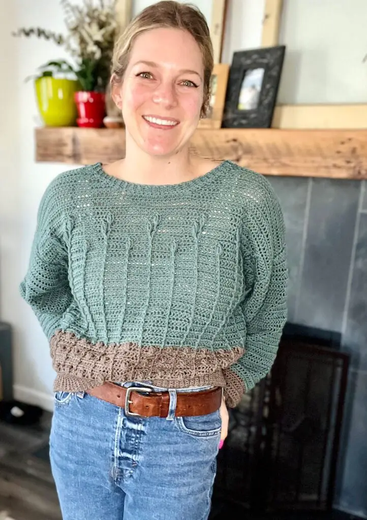 A woman wearing a turquoise and gray crochet sweater with a cabled floral pattern.