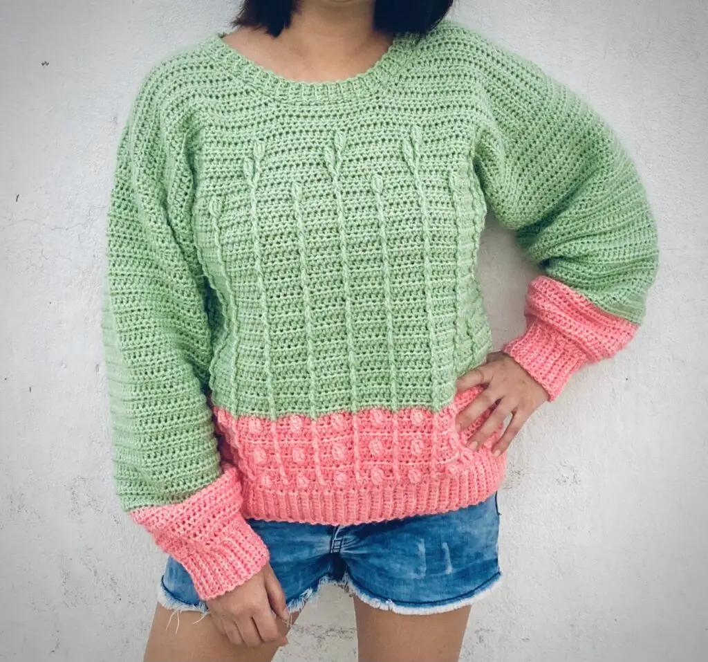 A woman wearing a mint and pink crochet sweater pattern.  Her hand is on her hip.