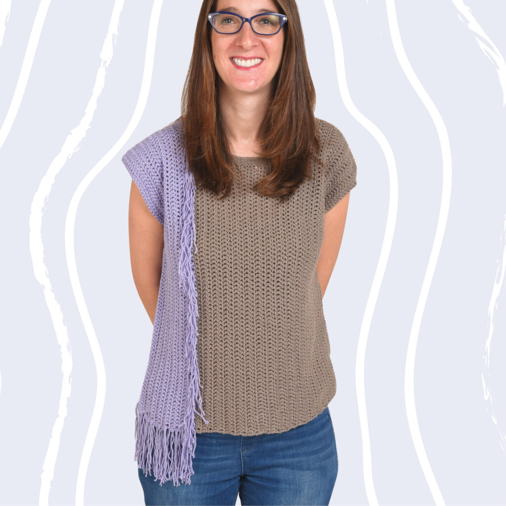 A woman wearing the Never Enough Fringe Crochet t shirt pattern.  This project will make a great addition to your crochet tops pattern collection.  It has color blocking on one side and fringe edges the color blocking.