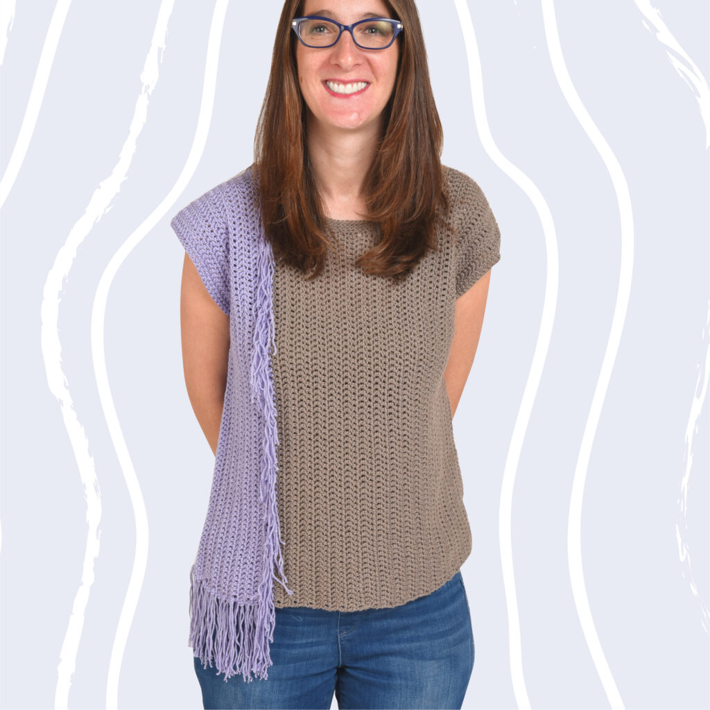 A woman wearing the Never Enough Fringe Crochet t shirt pattern. This project will make a great addition to your crochet tops pattern collection. It has color blocking on one side and fringe edges the color blocking.
