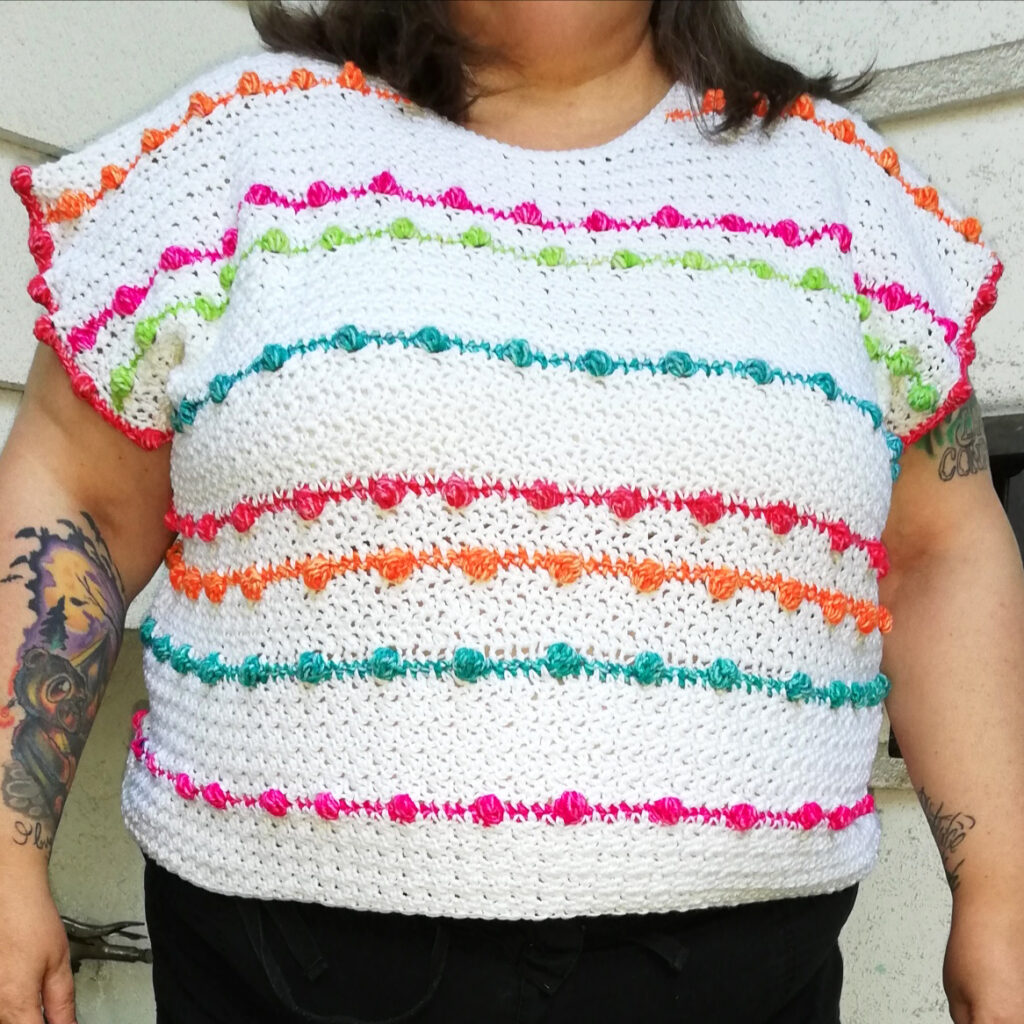 A custom Lean into Bobbles crochet top with multicolored bobble stitch stripes against a white crochet
