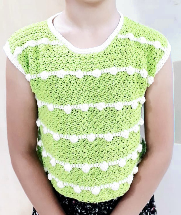 A lime green crochet t shirt with bobbles being worn by a child.