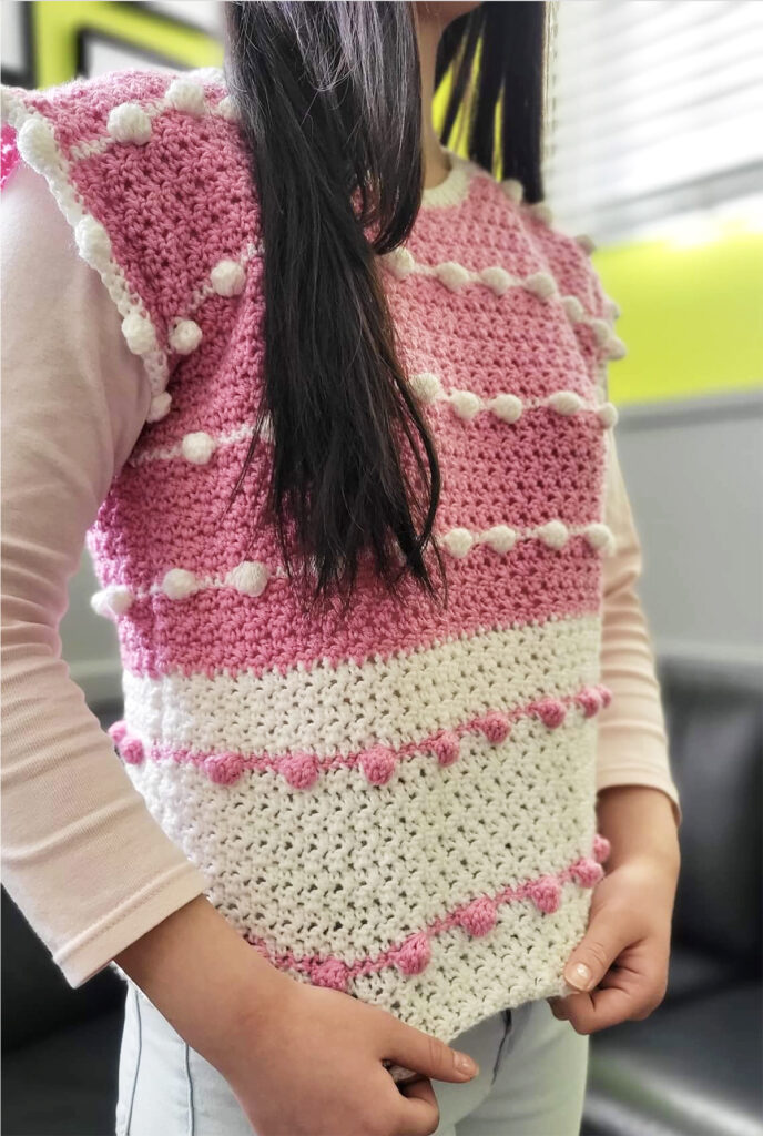 A pink and white crochet t shirt pattern featuring the bobble stitch and the griddle stitch being worn by a woman.