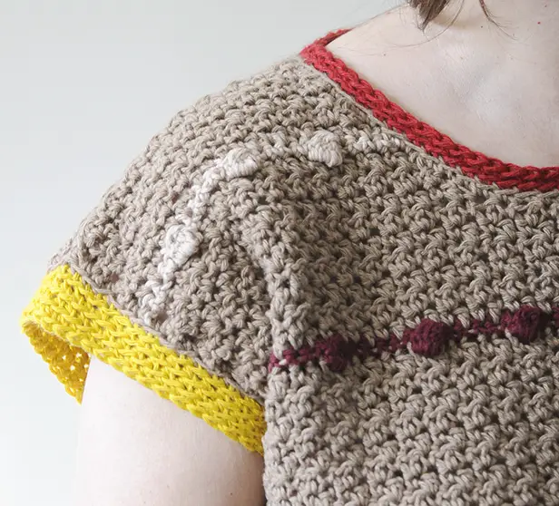 The shoulder of a brown crochet t shirt featuring colorful edging and a bobble stitch pattern stripe.