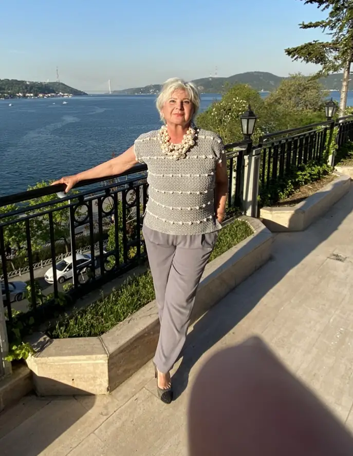 A woman standing, leaning on a fence overlooking water wearing a crochet top with bobble stitches and statement jewelry.