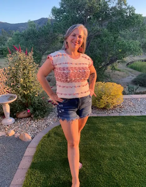 A woman wearing a pink and white crochet summer top pattern made with Lion Brands comfy cotton yarn.