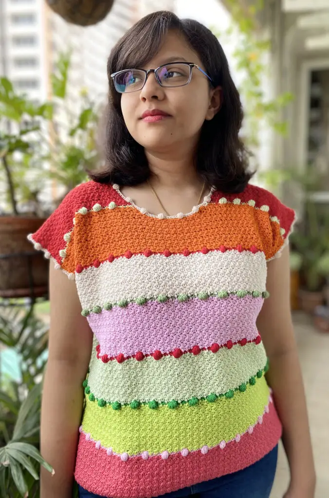 A woman wearing a brightly striped crochet top pattern in summer against an urban background.