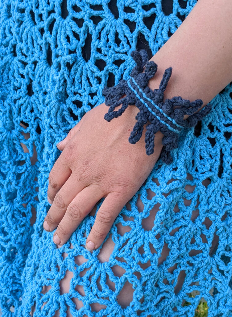 A woman's hand wearing a crochet bracelet resting on a crochet skirt.