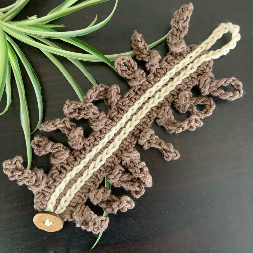 The Wild Knots Bracelet Pattern laying flat on a table with a bit of greenery. 