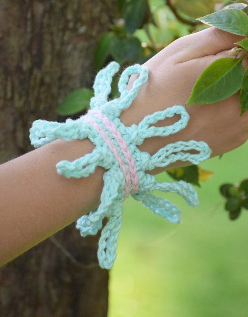 A woman's wrist wearing a pastel crochet bracelet featuring a knotted border.