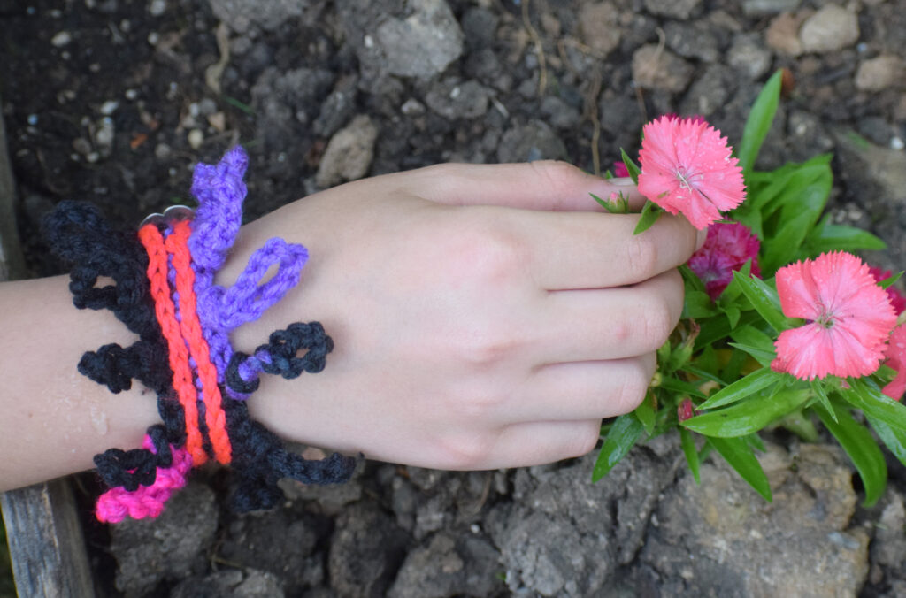 A woman's hand holding a pink flower.  She is wearing crochet jewelry.