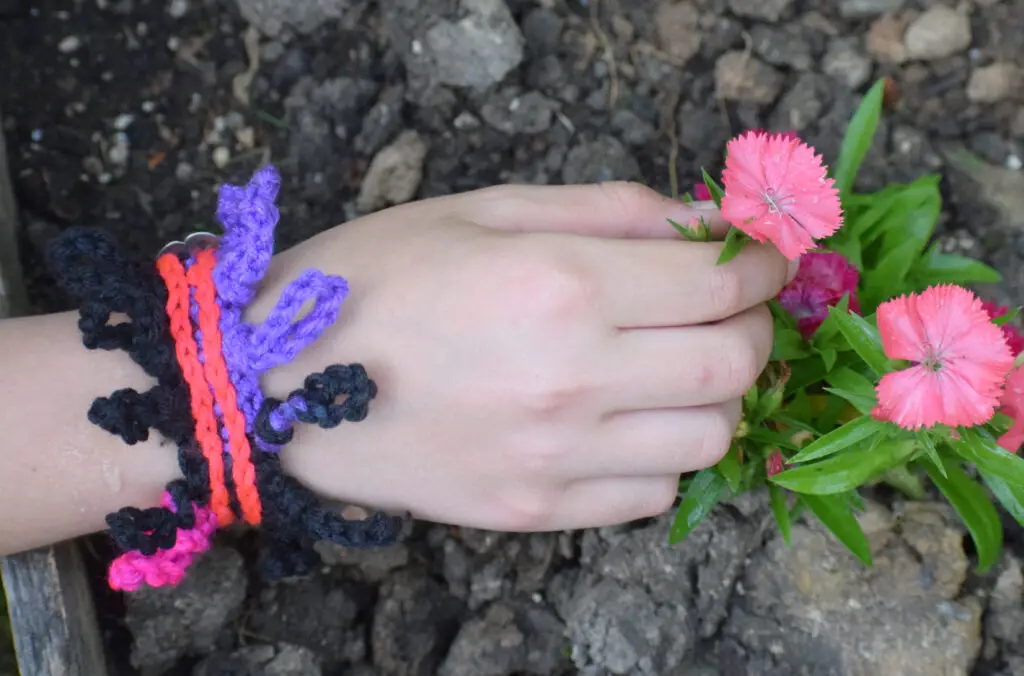 A woman's hand holding a pink flower.  She is wearing crochet jewelry.