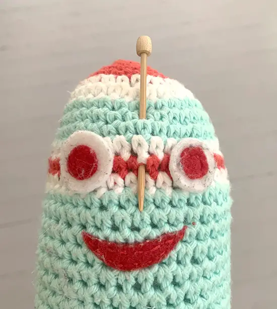 A crochet pin marks the middle of a face on an amigurumi robot.