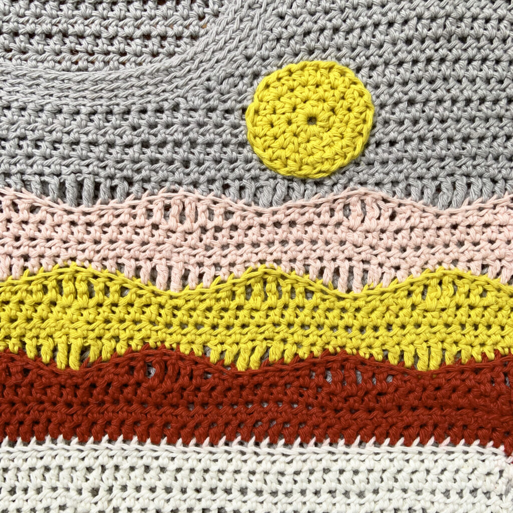 A close up of the Beautiful View Tee T shirt pattern.  Mountains and a sun are created with wave crochet stitches.