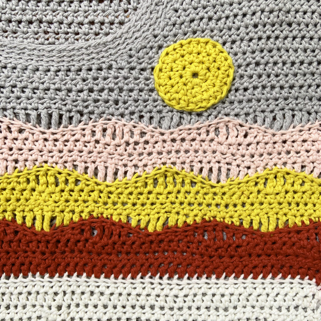 A close up of the Beautiful View Tee T shirt pattern. Mountains and a sun are created with wave crochet stitches.