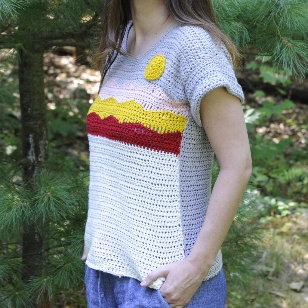A side view of a crochet top pattern depicting a mountain landscape and a sun.