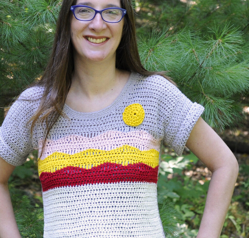 A woman wearing a crochet top pattern. The top has a picture of a mountain on it created in crochet stitches.