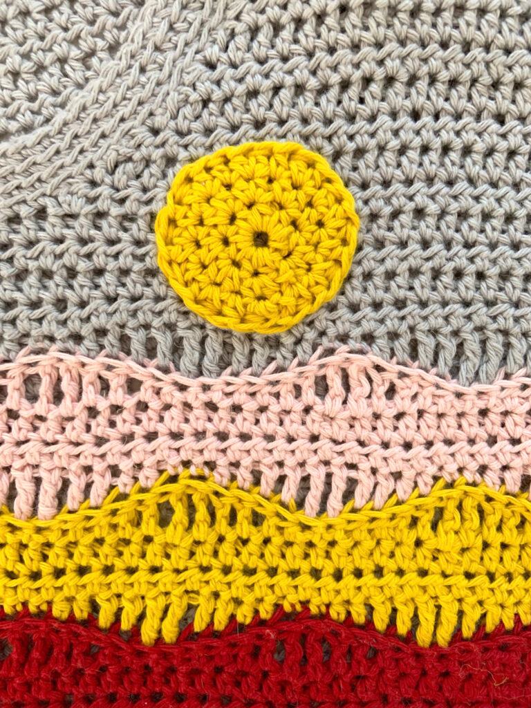 A close up of an applique applied to a crochet top with a running stitch.